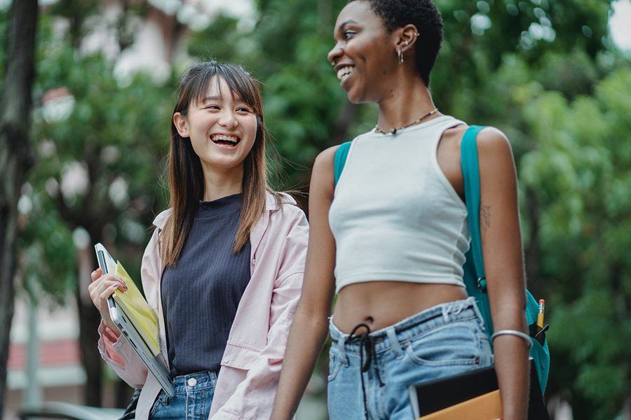 Two college students walking outside of a college holding books and laughing